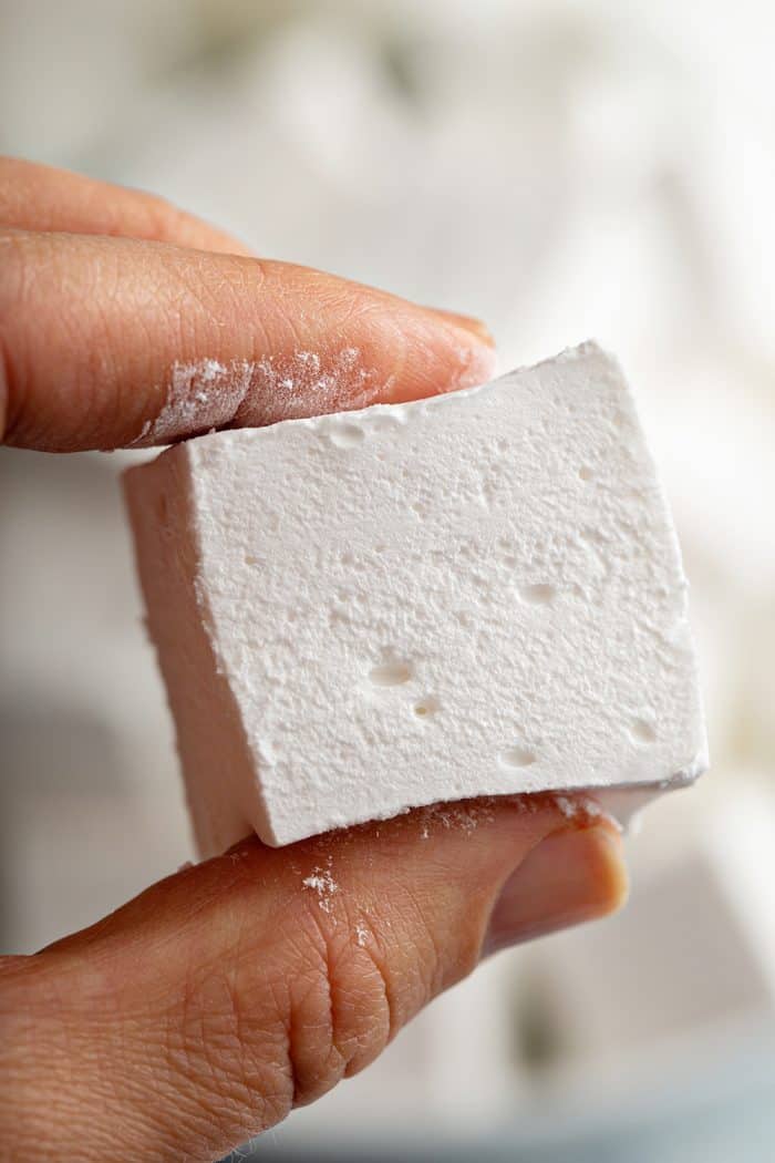 Hand holding up a homemade marshmallow to show the soft texture