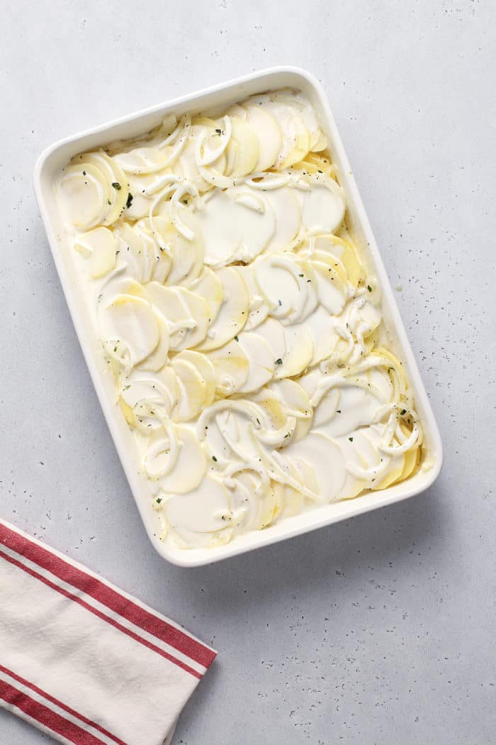 Prepped scalloped potatoes in a white baking dish, ready to go in the oven