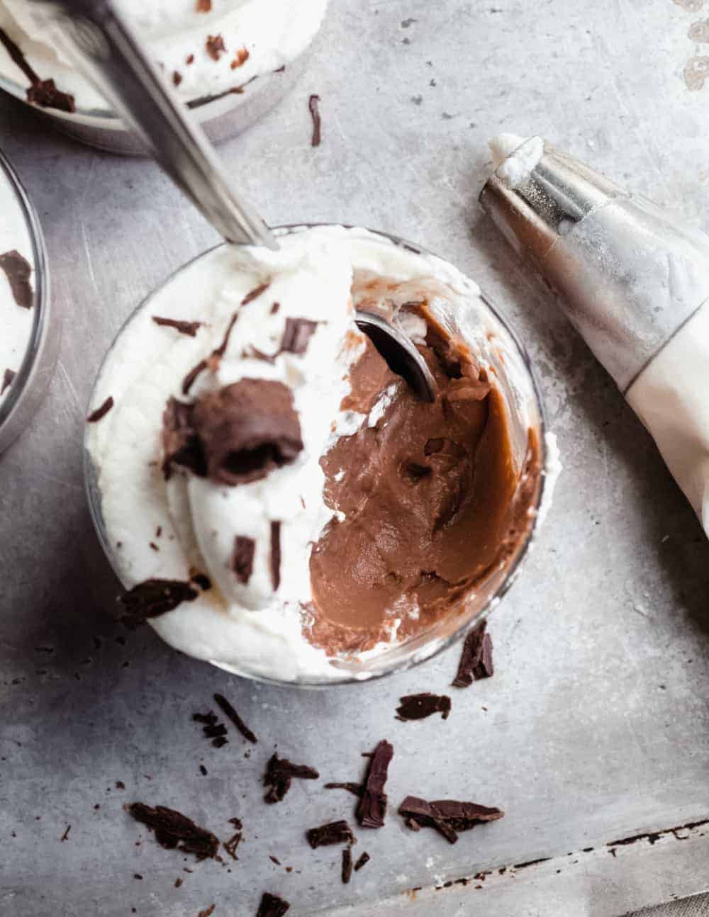 Close up of homemade chocolate pudding topped with whipped cream next to a piping bag of whipped cream