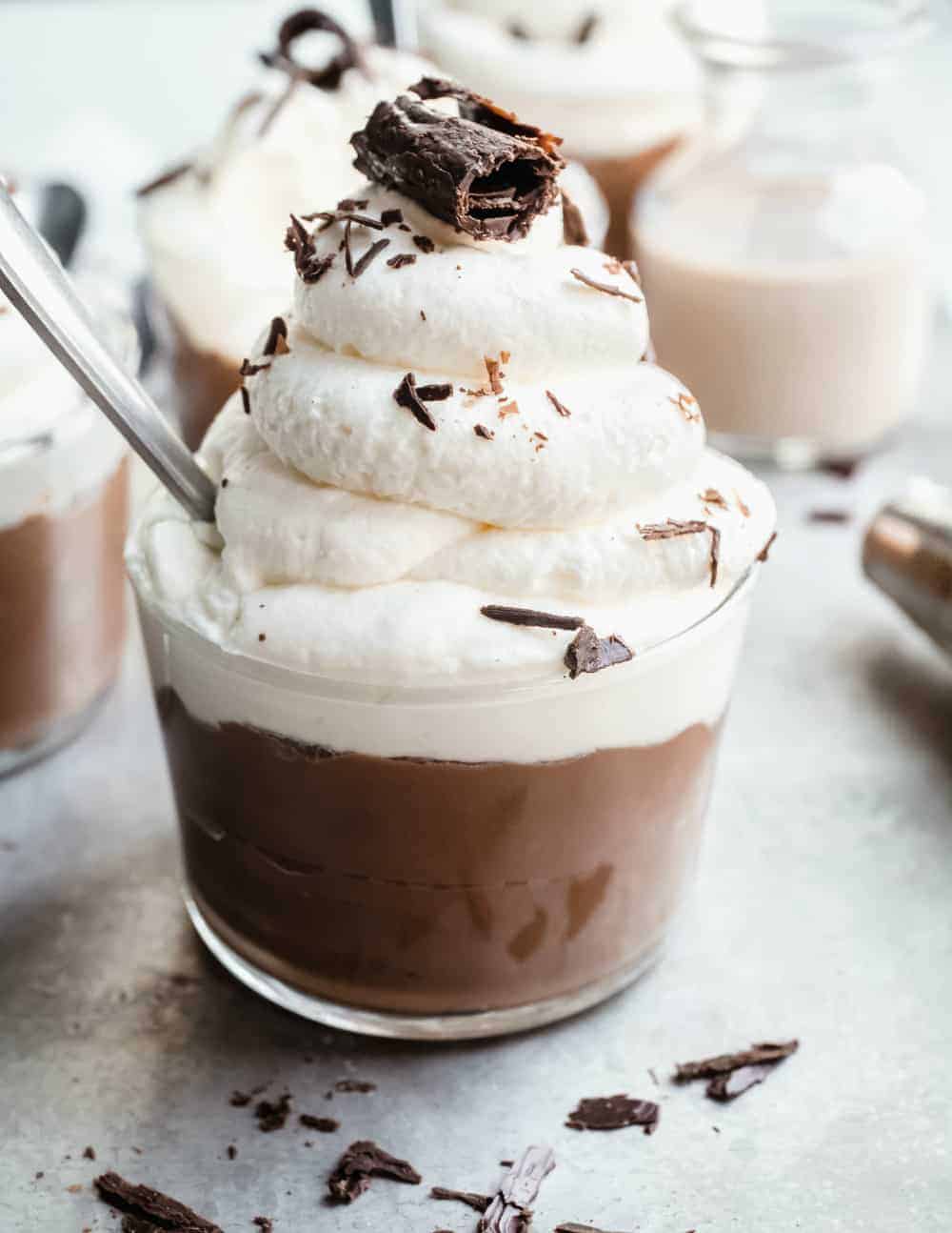 Close-up side view of homemade chocolate pudding in a glass cup, topped with whipped cream and chocolate shavings