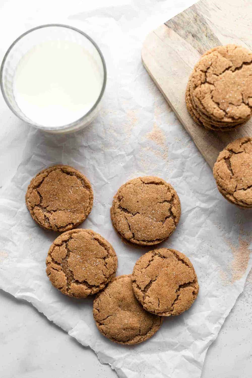 Glass of milk next to chai sugar cookies scattered on a piece of parchment paper