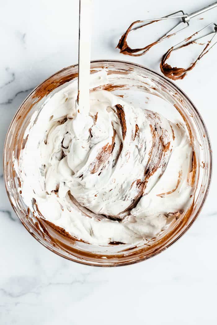 Spatula folding frozen whipped topping into the base for no bake nutella cheesecakes in a glass mixing bowl