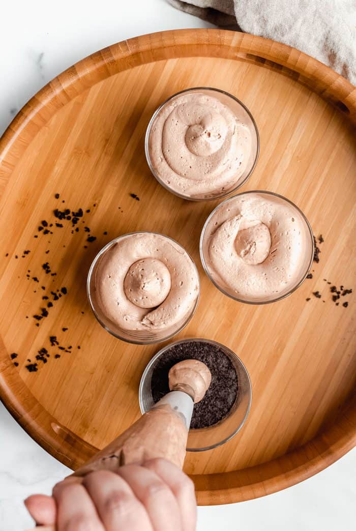 Overhead view of piping bag piping nutella cheesecake filling onto oreo crusts in individual serving dishes