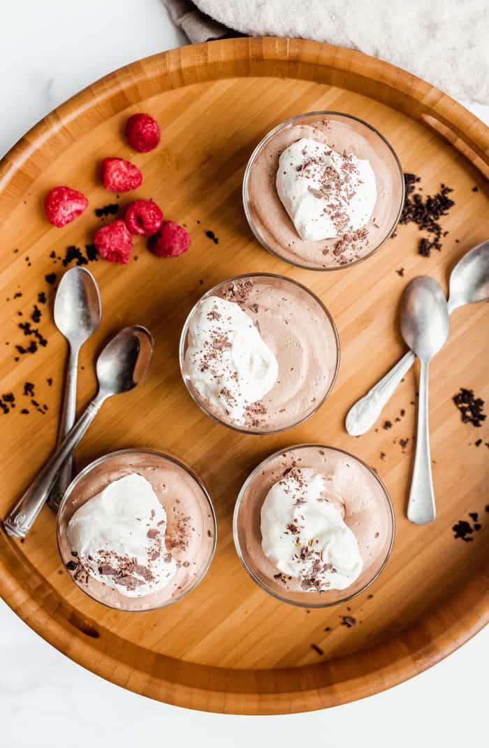 Overhead view of no bake nutella cheesecakes in ramekins on a wooden board next to spoons and raspberries