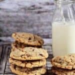 Stacks of toffee almond cookies on a cooling rack with a glass of milk