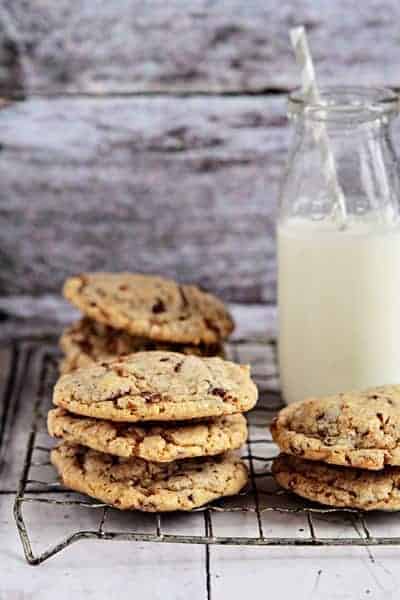 Stacks of toffee almond cookies on a cooling rack with a glass of milk