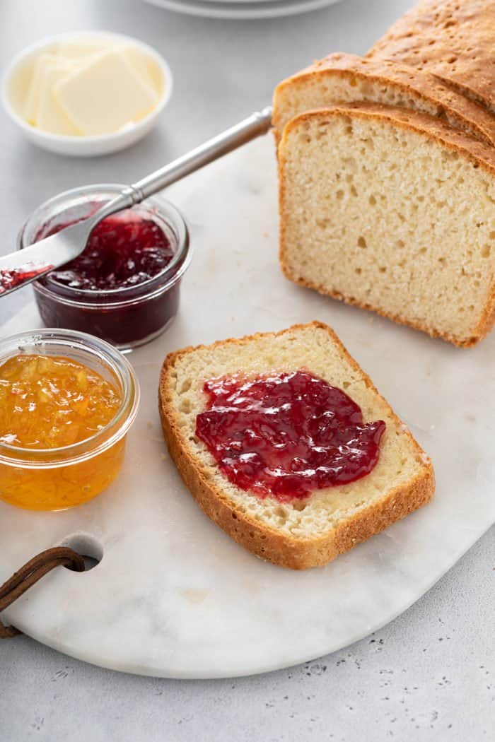 Slice of english muffin bread topped with jam set next to two small bowls of jam