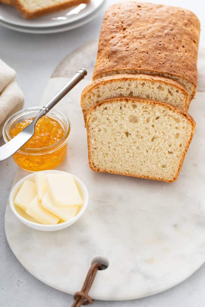 Sliced loaf of English Muffin Bread next to butter and jam on a marble board