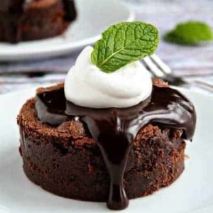 A mint brownie on a round plate topped with hot fudge, whipped cream, and a fresh mint leaf