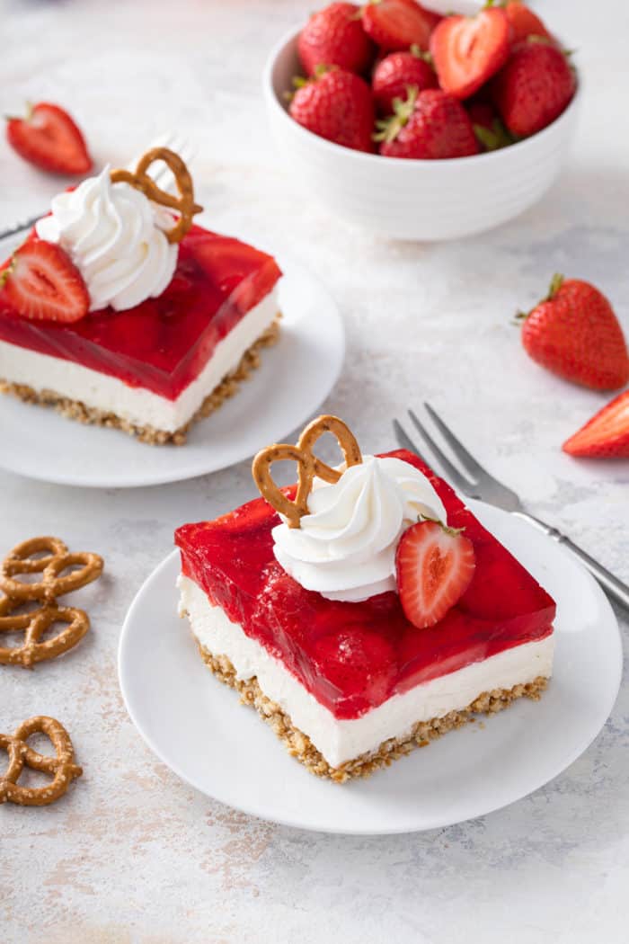 Two white plates, each with a slice of strawberry pretzel salad, set on a light-colored countertop.