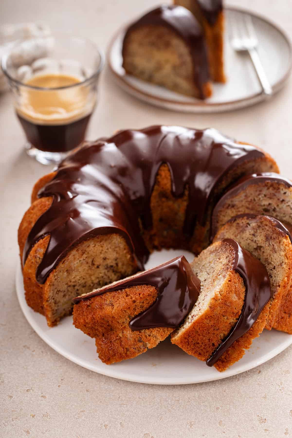 Sliced banana bundt cake topped with chocolate ganache on a white cake plate.