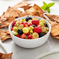 White bowl of fruit salsa with cinnamon chips in the background.