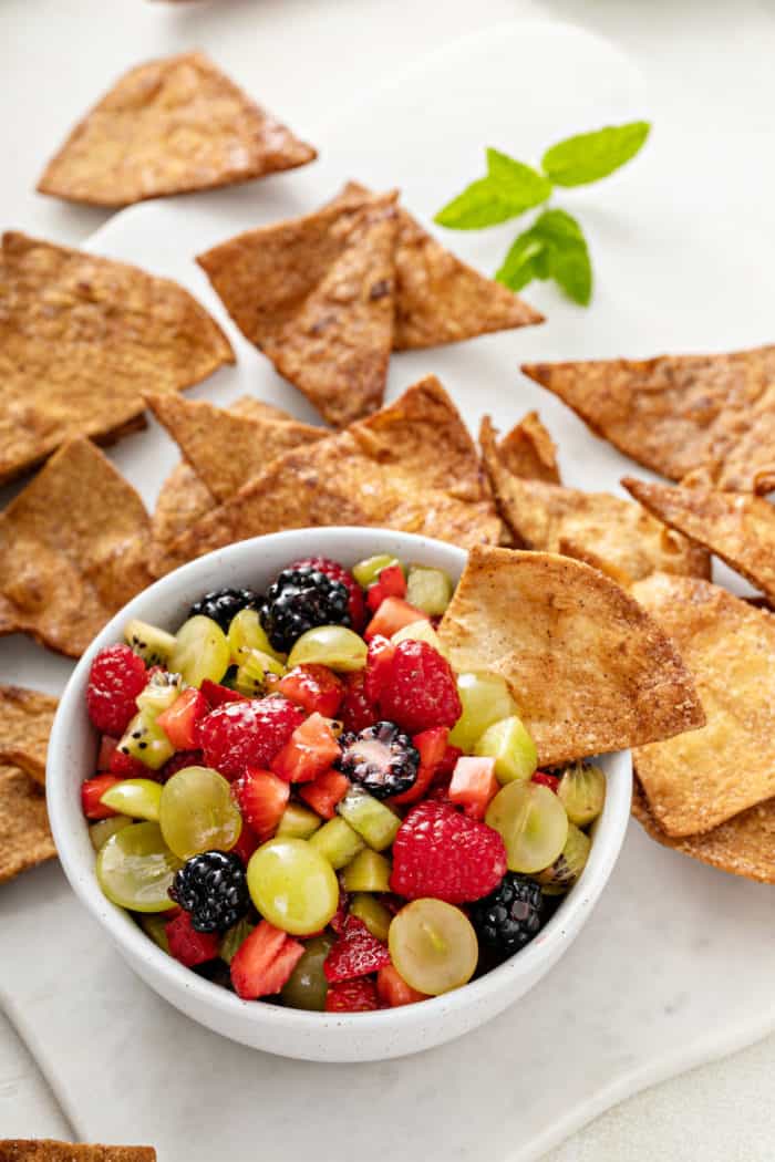 Cinnamon chip in a bowl of fruit salsa, with more cinnamon chips in the background.