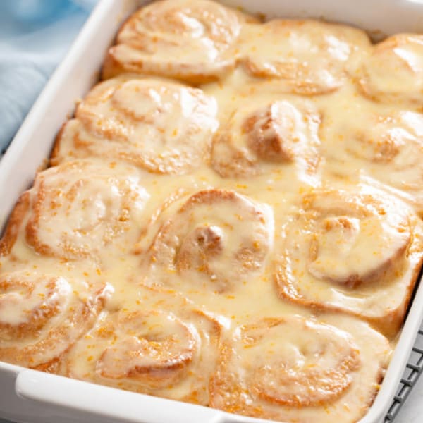 White baking dish filled with baked and glazed orange rolls.