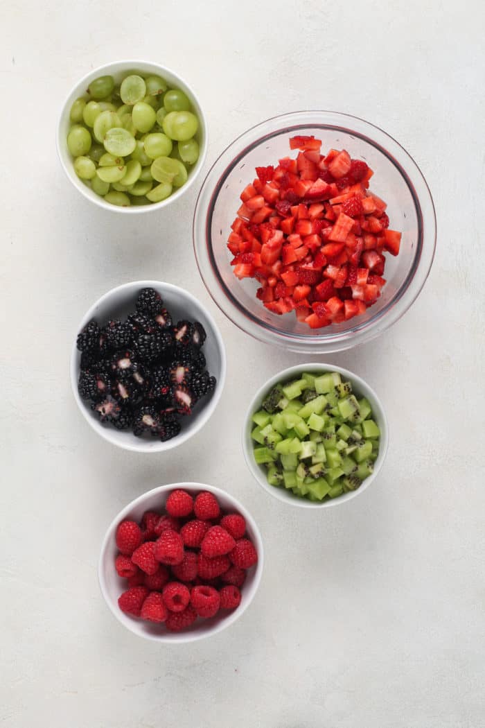 Bowls of diced fresh fruit for fruit salsa arranged on a white countertop.