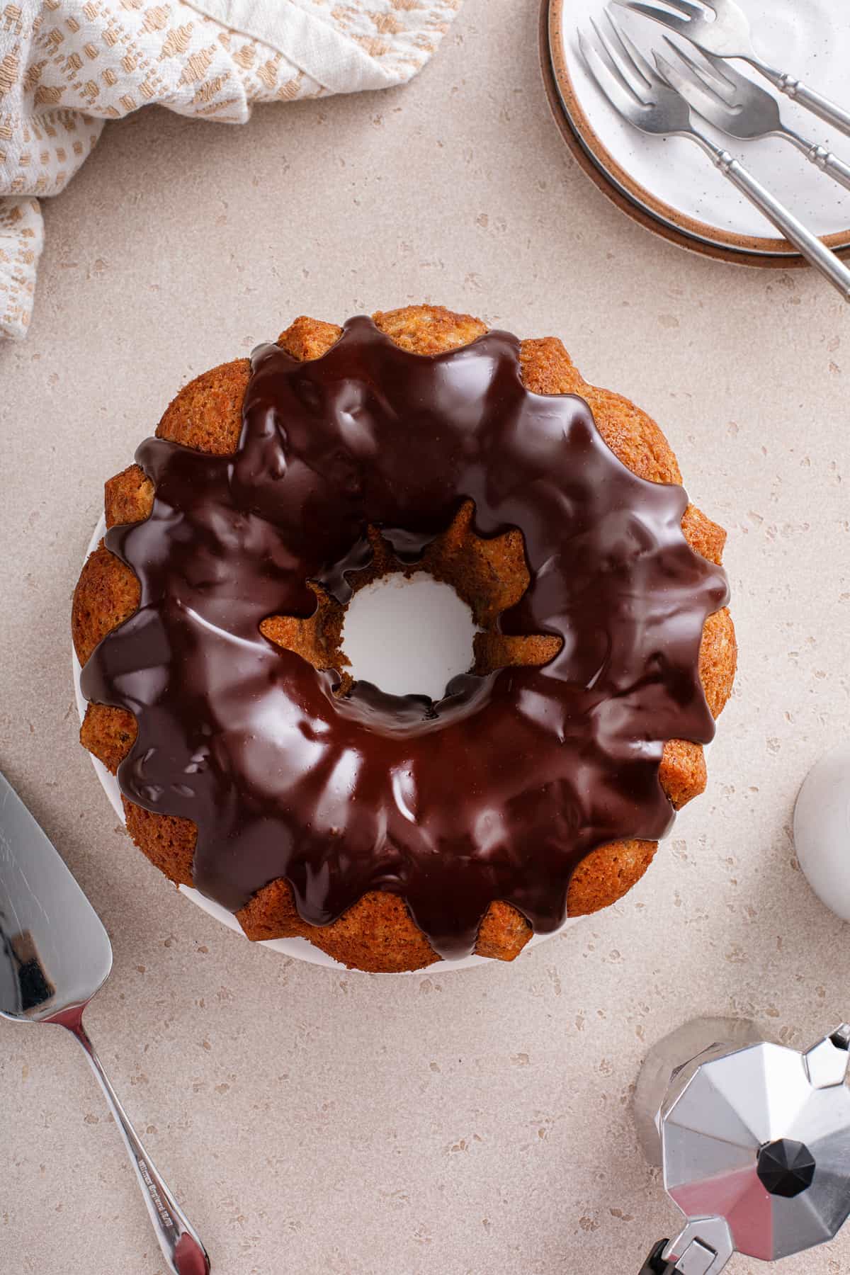 Banana bundt cake topped with ganache, set on a white cake plate.