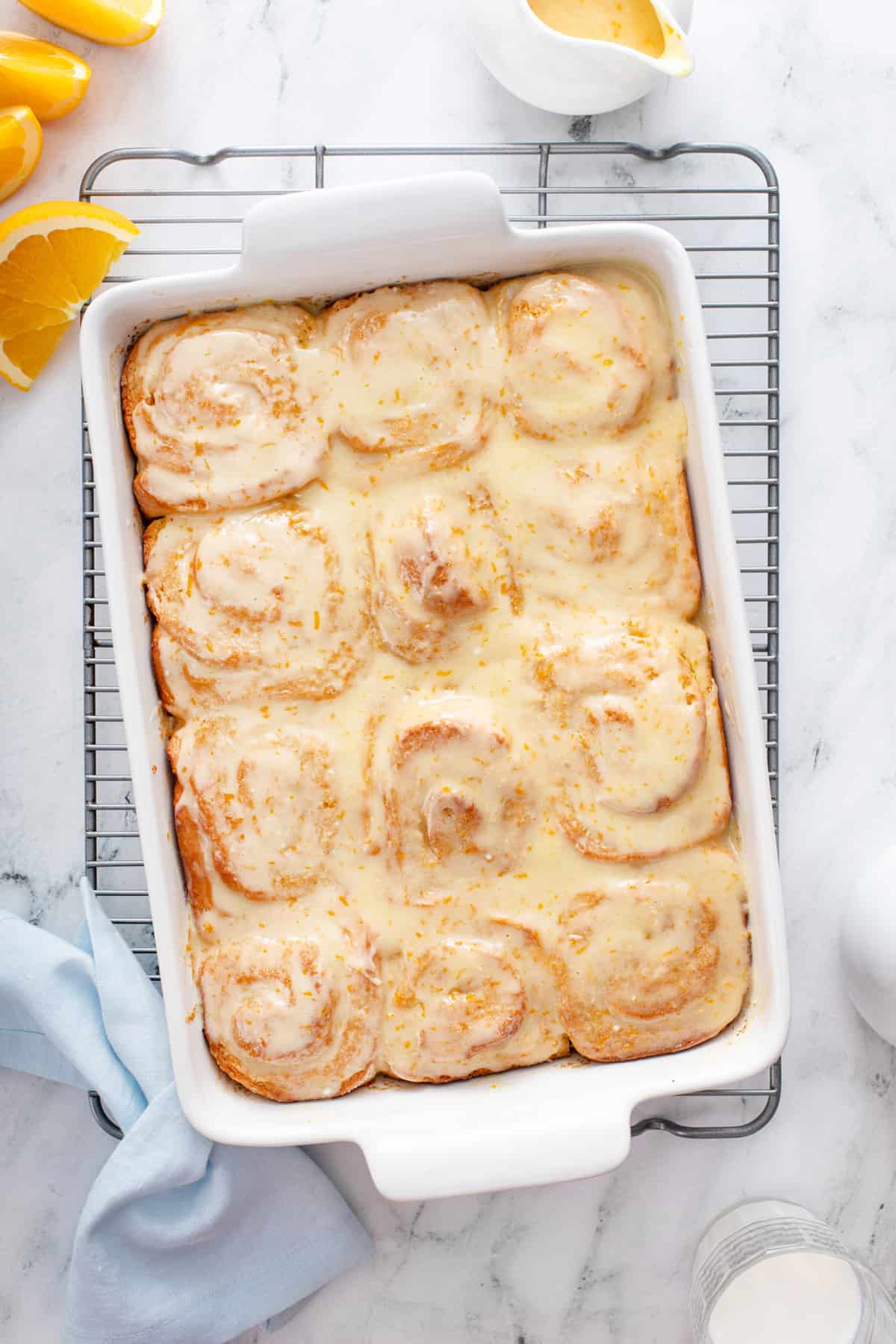 Overhead view of glazed sticky orange rolls in a white baking dish, set on a wire cooling rack.