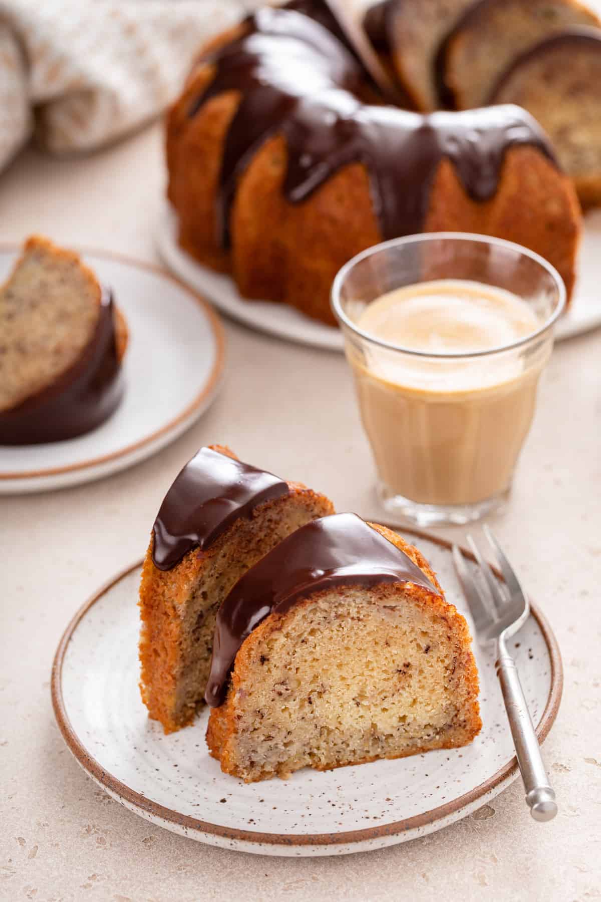 Two ganache-topped slices of banana bundt cake next to a fork on a plate.