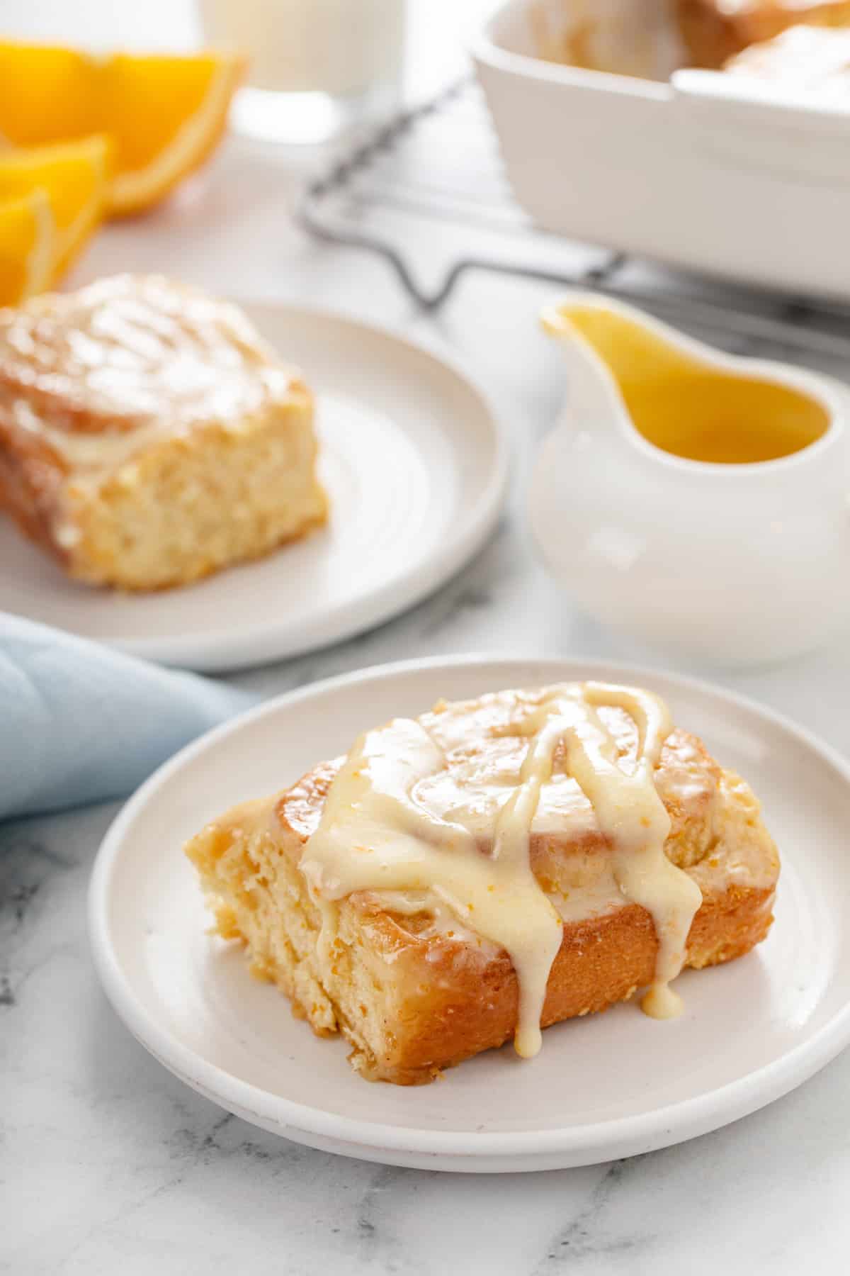 Two white plates holding sticky orange rolls, with a small pitcher of orange glaze in the background.