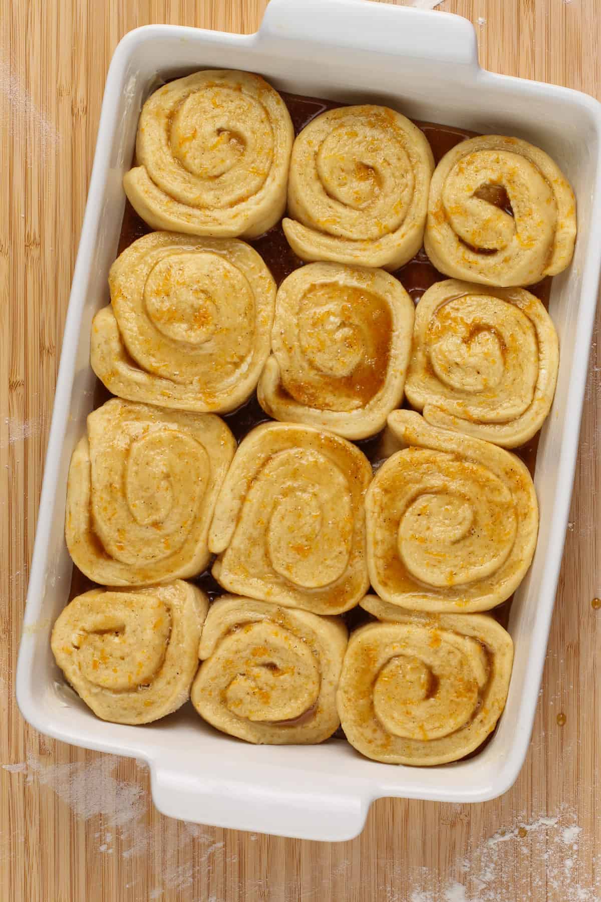 Risen orange rolls in a white baking dish, ready to go in the oven.