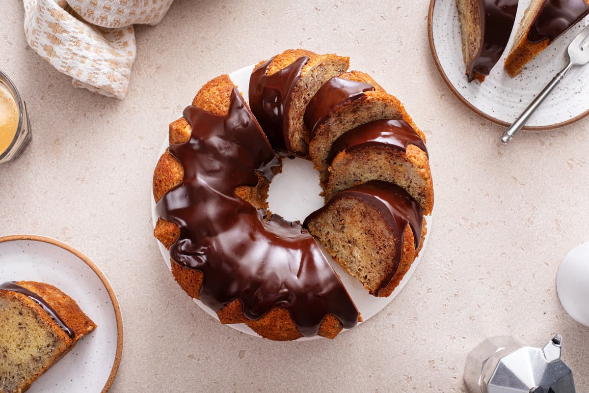Overhead view of ganache-topped and sliced banana bundt cake on a white cake plate.