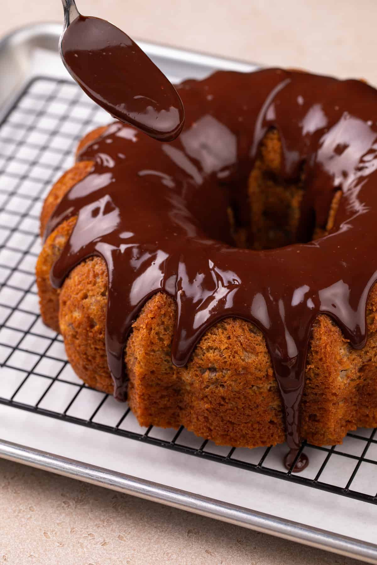 Spoon pouring chocolate ganache over banana bundt cake.