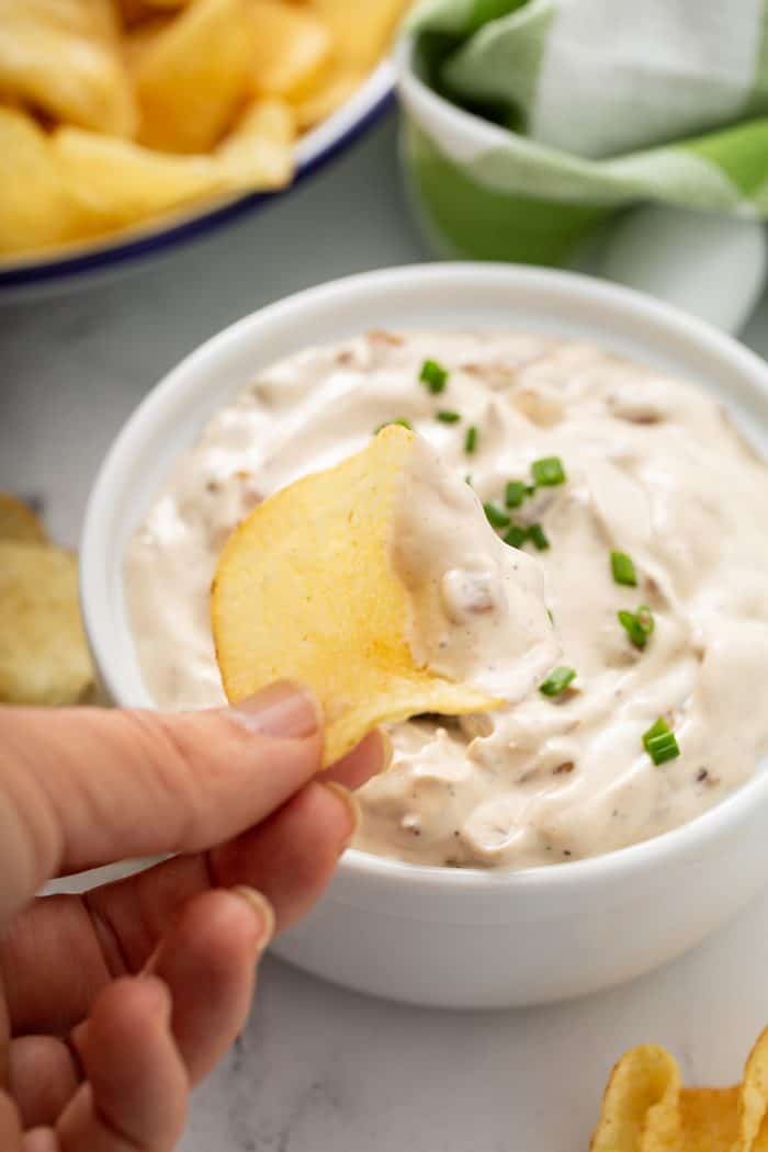 Hand scooping up french onion dip with a potato chip