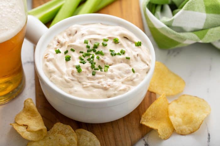 Bowl of french onion dip on a wooden board surrounded by potato chips