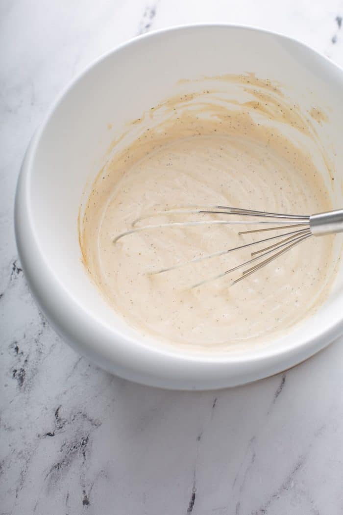 Whisk combining sour cream, mayo, and seasonings in a white mixing bowl