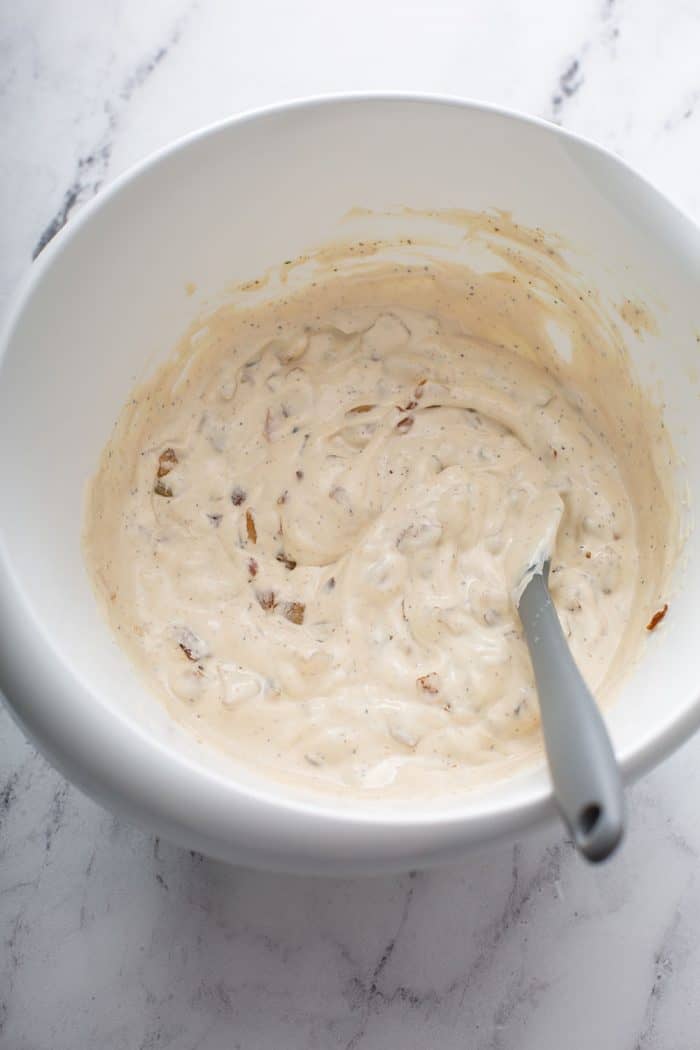 Spoon stirring french onion dip in a white bowl