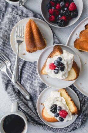 Slices of 7up pound cake on an assortment of white plates, topped with whipped cream and berries