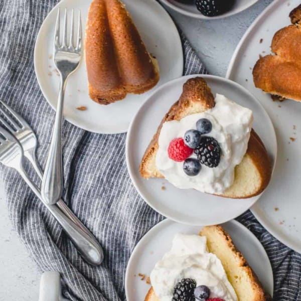 Slices of 7up pound cake on an assortment of white plates, topped with whipped cream and berries