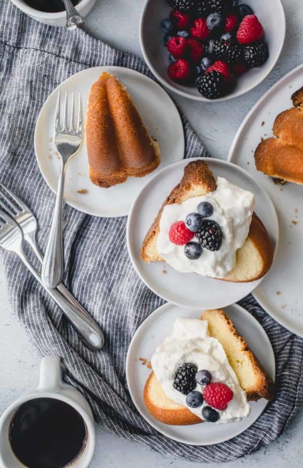 Slices of 7up pound cake on an assortment of white plates, topped with whipped cream and berries