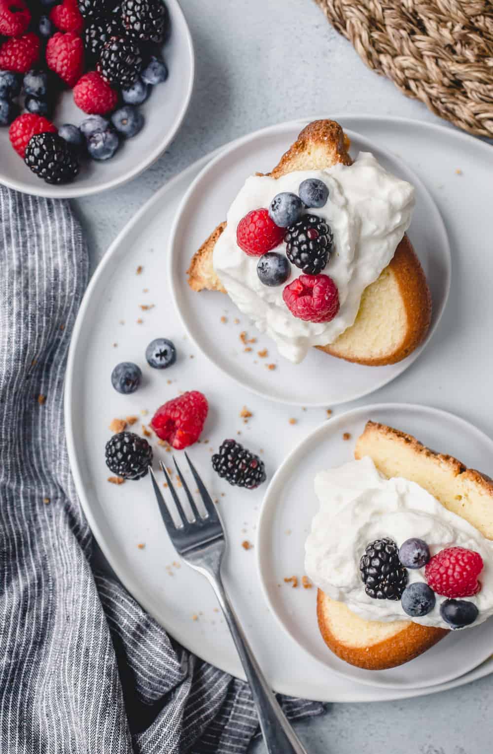 Two slices of 7up pound cake on white plates, topped with whipped cream and fresh berries