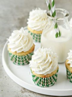 Coconut cupcakes on a round white plate with a glass of milk in the center