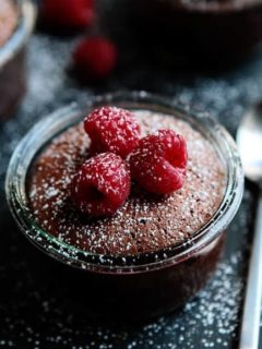 Close up of flourless chocolate cake topped with raspberries and dusted with powdered sugar