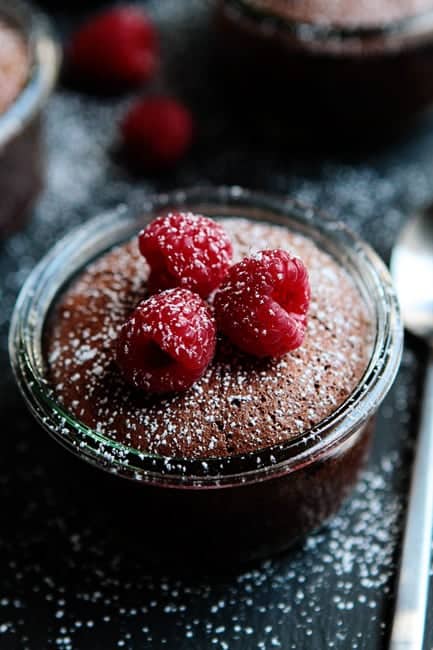 Close up of flourless chocolate cake topped with raspberries and dusted with powdered sugar