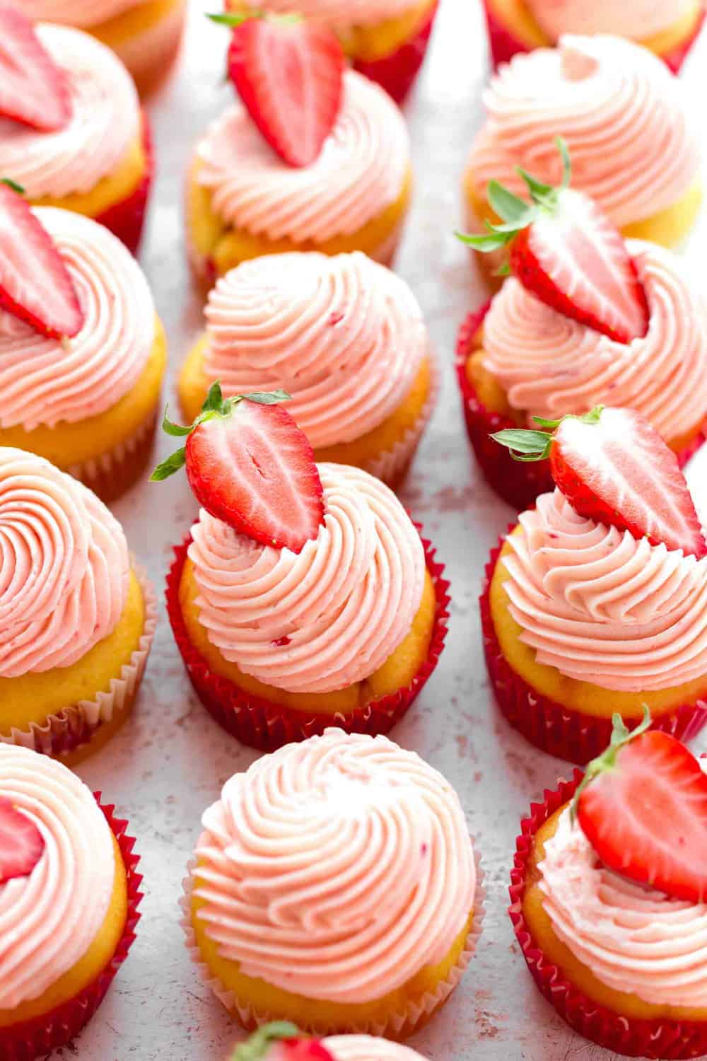 45-degree view of cupcakes topped with strawberry buttercream and halved strawberries on white surface
