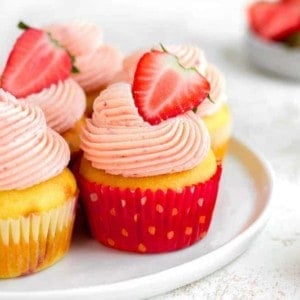 Side view of easy strawberry cupcakes on a white plate, topped with halved fresh strawberries