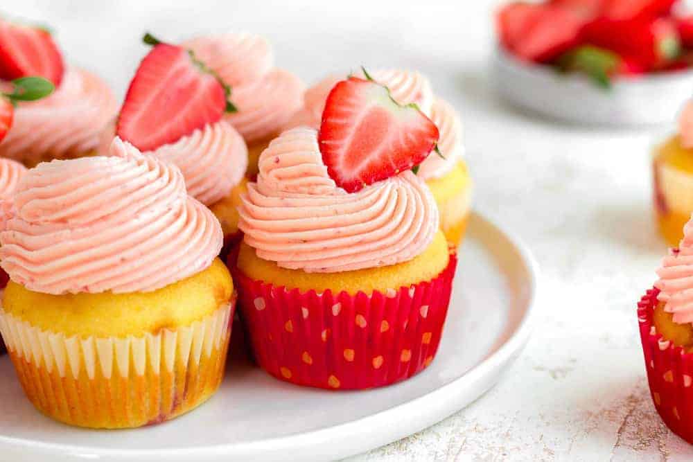 Side view of easy strawberry cupcakes on a white plate, topped with halved fresh strawberries