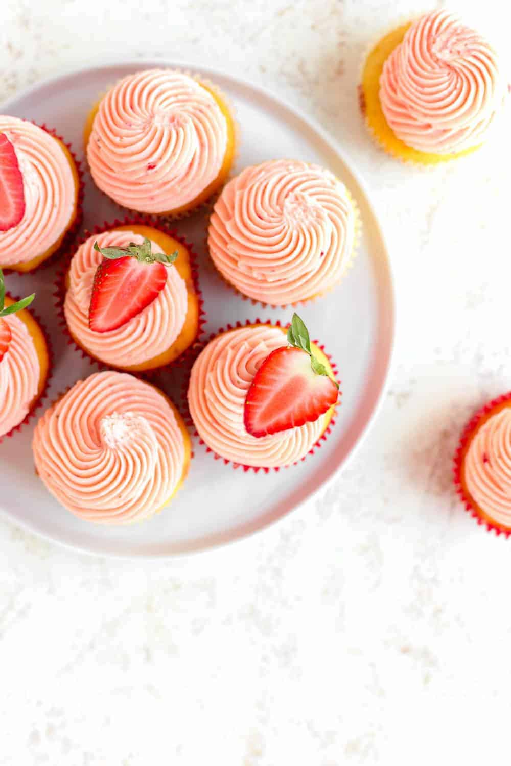 Overhead shot of easy strawberry cupcakes on a white plate, topped with halved strawberries