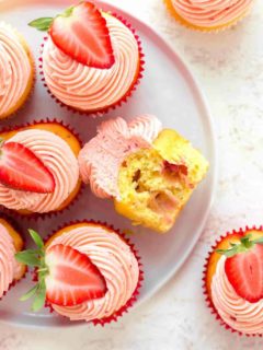 Overhead view of easy strawberry cupcake with a bite taken out of it on a white plate, surrounded by other strawberry cupcakes