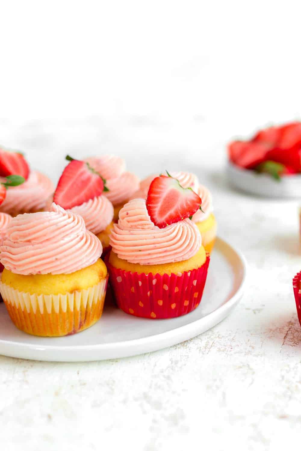 Side view of easy strawberry cupcakes topped with strawberry buttercream on a white plate
