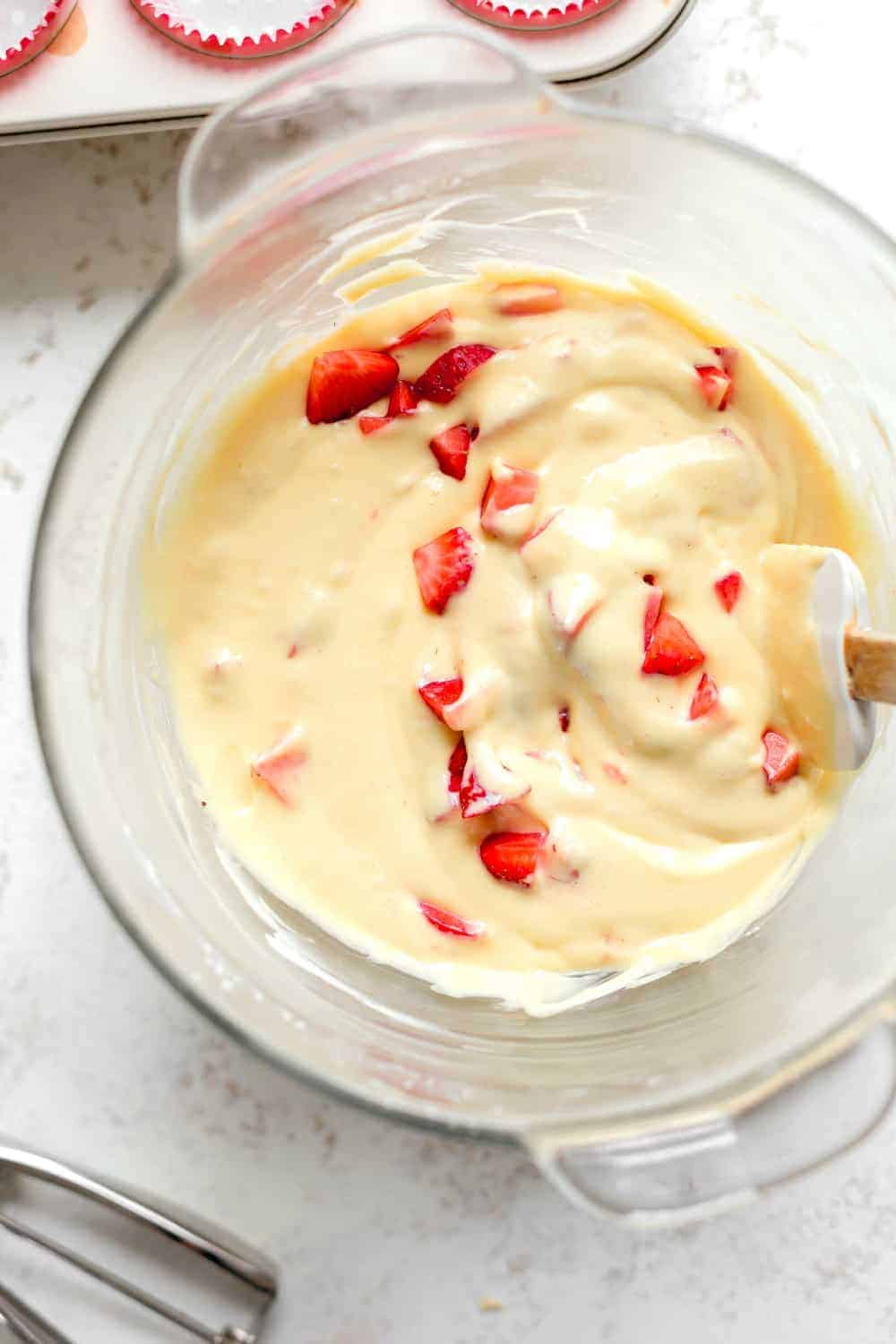 Overhead view of diced strawberries mixed into cupcake batter in glass bowl