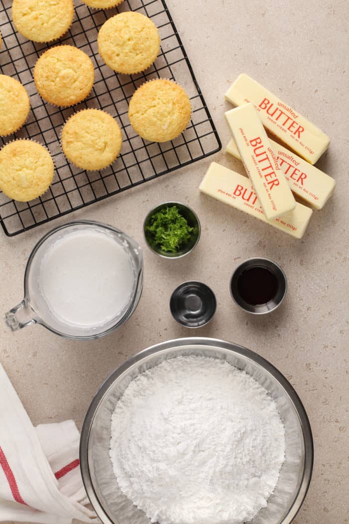 Coconut-lime frosting ingredients next to coconut cupcakes on a wire cooling rack.