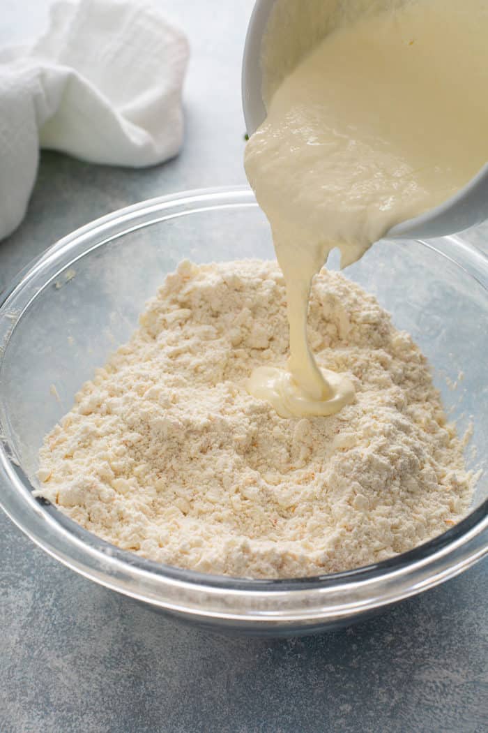 Wet ingredients being added to the dry ingredients for orange scones in a glass mixing bowl