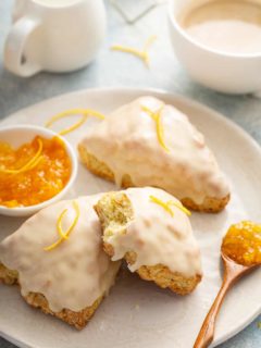 Orange scone with a bite taken out of it stacked on top of two other scones on a white plate