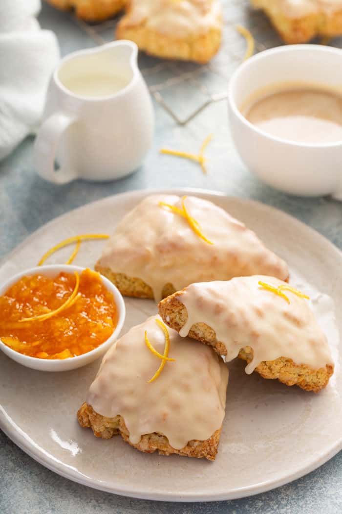 Three glazed orange scones on a white plate next to a ramekin of orange marmalade