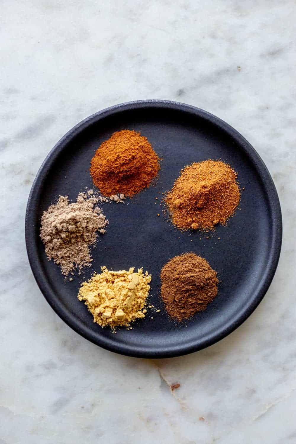 Spices for apple pie spice on a black plate
