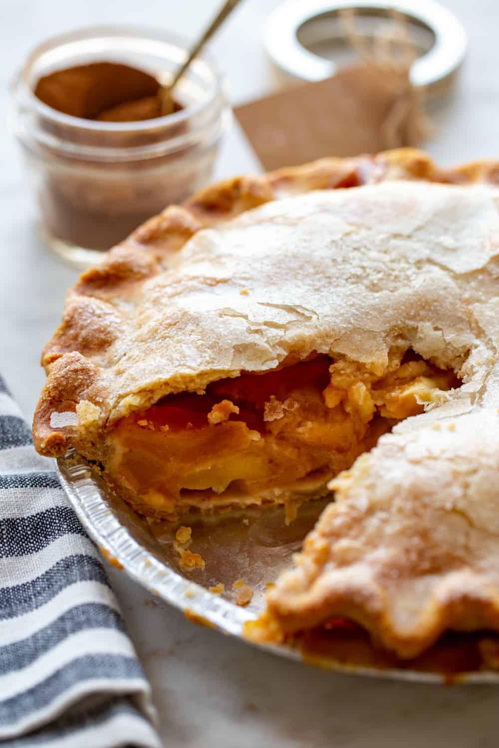 Apple pie with a slice missing in front of a jar of apple pie spice